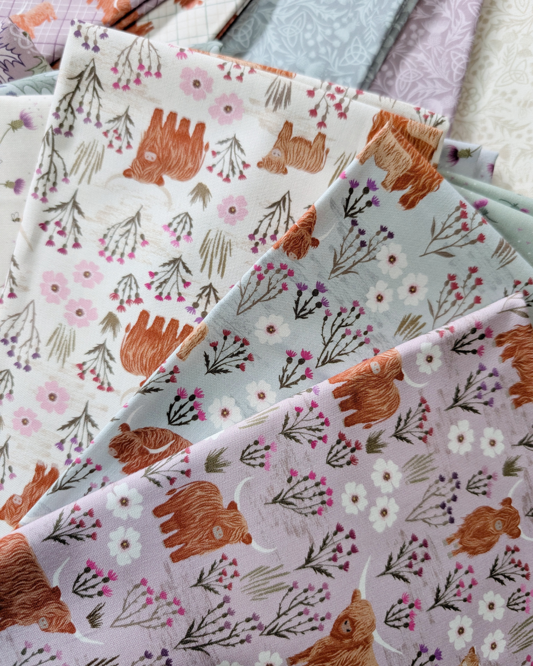 Summer Meadow Highland cut fabric from A Celtic Summer collection by Lewis & Irene features Highland cows and Scottish thistle in shades of Cream, Breezy Blue, and Light Heather.