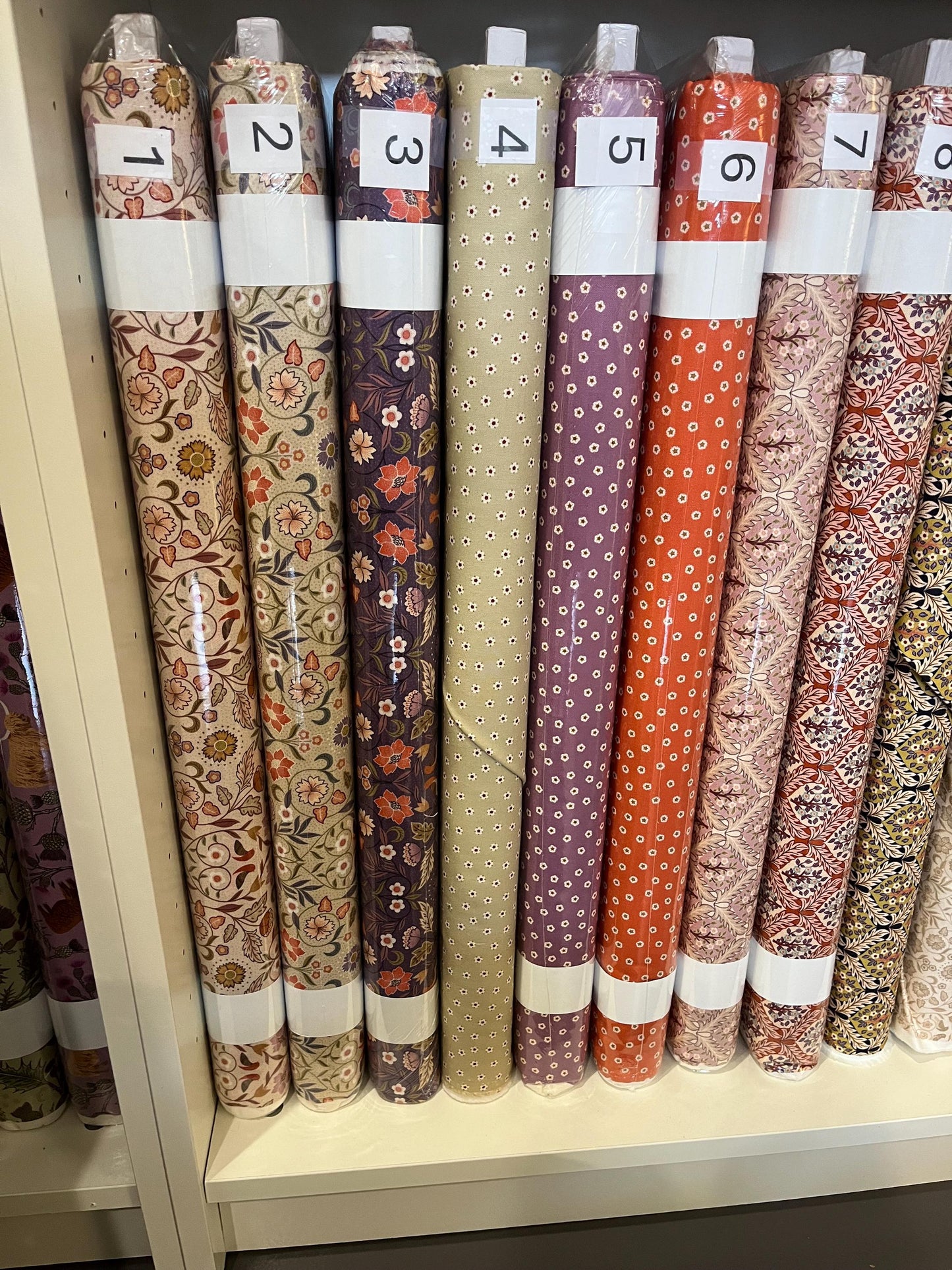 Bolts of arts and craft patterned fabric from the Isabella Collection by Lewis and Irene, labeled one through seven.