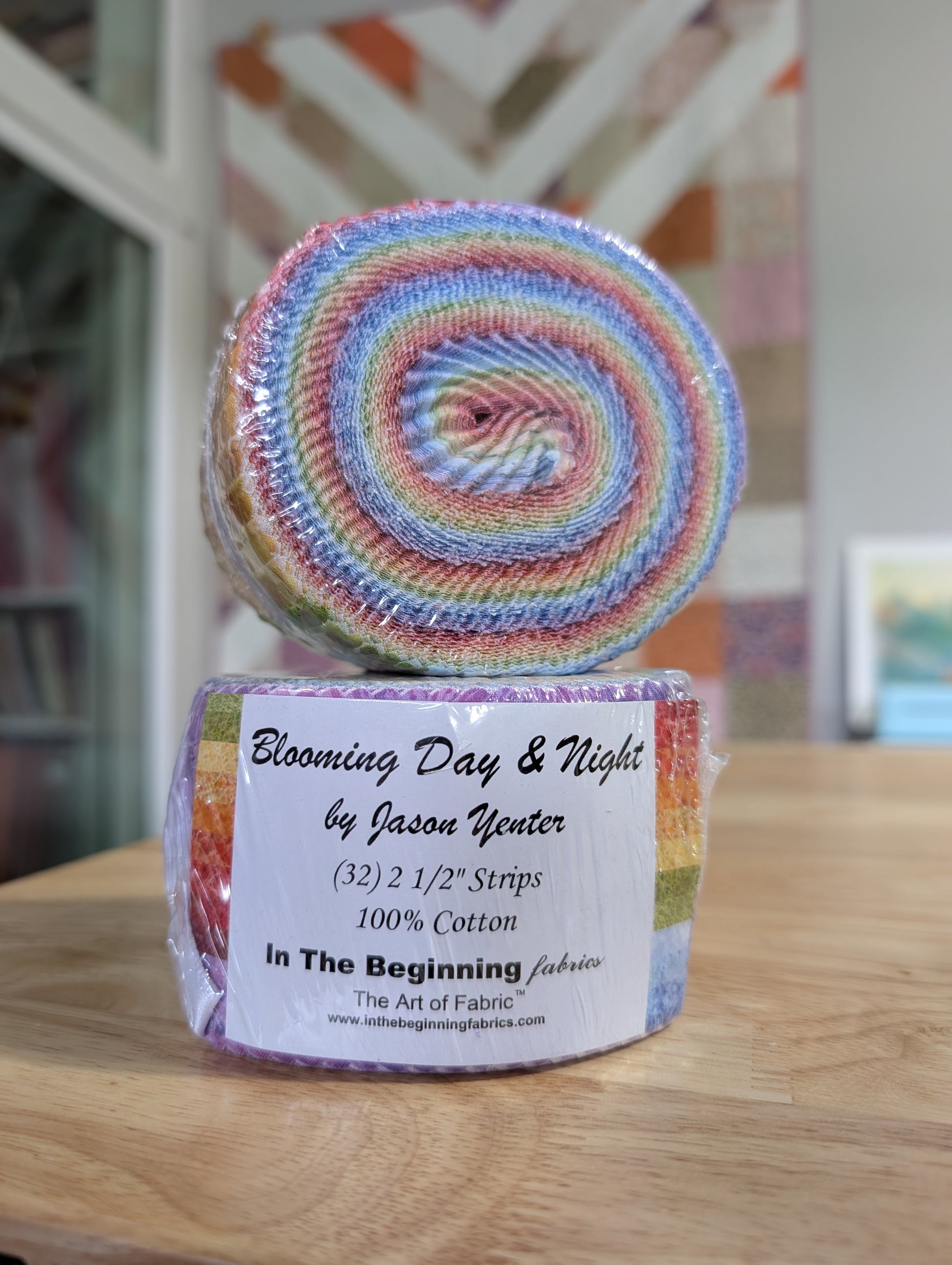 A rolled and packaged cotton quilting fabric bundle labeled 'Blooming Day & Night by Jason Yenter' sits on a wooden surface with a softly blurred indoor background.